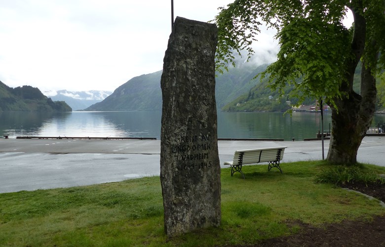 Minnesteinen i Vadheim over to falne i andre verdskrigen står i sentrum ved kaia og buss-stoppestaden. Framsida vender mot fjorden.