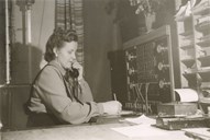 Steinklepp (Borgund) telefonsentral var kombinert med postopneri. Kari Maristuen (f.1923) sit ved sentralbordet og har postbordet til høgre. Skrankeluka var bak ryggen hennar.