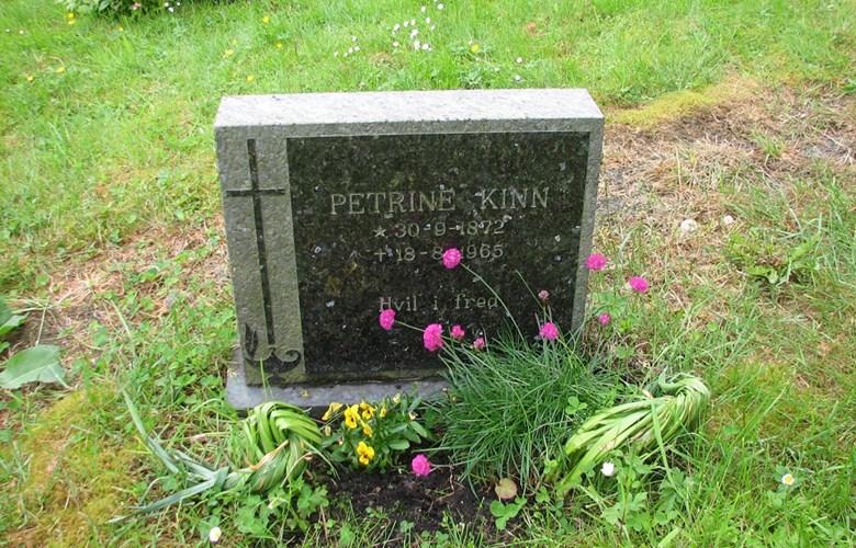 Grava til Petrine Kinn med minnestein oppsett i 1985. Blømande strandnellikar og stemorsblomar ber bod om at grava blir stelt om. Blada til påskeliljene er ikkje klypte av, men knytte i kvileposisjon.