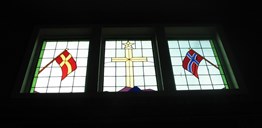 Vindauga på veggen framme i storsalen har innfelt kross flankert av krossmerkte flagg.