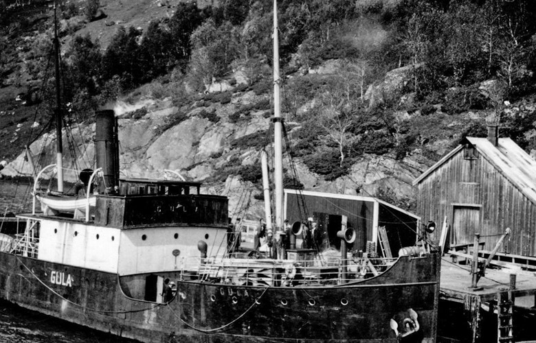 DS «Gula» til kai ved Holand i Holandsfjorden, Meløy kommune. Originalfotografiet finst i fotosamling etter Egil Furuhatt. Under krigen 1940-1945 var familien Egil Furuhatt evakuert frå Bodø til Holandsfjorden, Meløy kommune. Furuhatt fotograferte, og det er mykje truleg Egil Furuhatt som har teke biletet.
