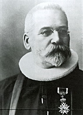 Portrettfoto av ein mann med briller, gamaldags prestekrage og medalje.