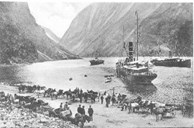 Dampskip til kai i Gudvangen, og hestekjerrer klare til skyss oppover Nærøydalen ein dag i 1912.  
 