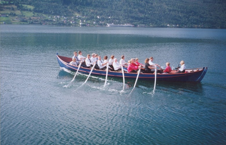 Kyrkjebåten "Rols" på fjorden med 12 personar ved årane.