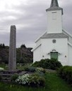 Vêrhardt og vend mot havet står minnesteinen ved Husøy kyrkje.