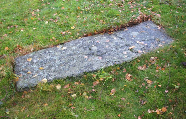 Mellomaldergravminnet ved Ortnevik kyrkje 2006. Steinen ligg heilt plant med bakken, og det er teikn til overgroing.

