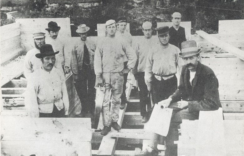 Arkitekt og byggmeister Lars Sølvberg sitjande lengst til høgre. Her er han og arbeidarane hans i gang med bygginga av Gloppens Sparebank i 1893.