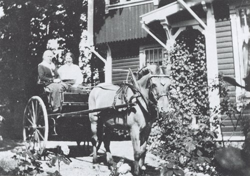 Bilete av miss Abbott til venstre og Margit Sahlgaard Børresen til høgre i ei hestekjerre framføre villaen som miss Abbott bygde.