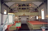 Kyrkjerommet sett frå koret mot galleriet og våpenhuset. Galleriet og benkene er måla i same grønfargen. Den øvste ryggstøtta på benkene er måla i ein raudbrum farge. Orgelet, som kom til kyrkja i 1955, stod tidlegare i ei kyrkje på Møre.
