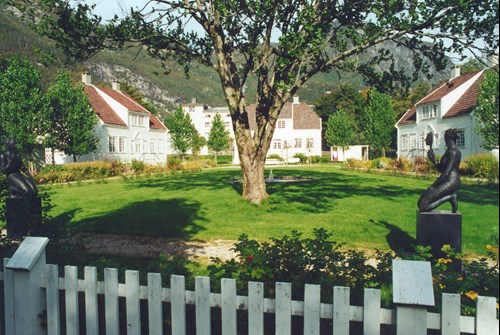 Bilete av grøntområde mellom husa, med skulputuren "Maskeberere" av Hidle Mæhlum.