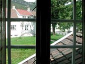 Frå vindauga i ein av bygningane ser ein ut på grøntområdet mellom husa og over til huset på den andre sida av plenen.
